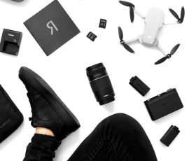 Top view of drone, camera gear, and accessories with a person in black clothing on a white background.
